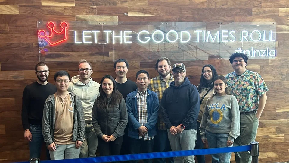 Members of the Bensinger Lab during an outing to a bowling alley stand under a neon sign that reads, "Let the good times roll."